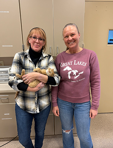 Two women smiling in a room, one holding a small dog.