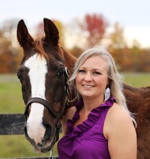 Woman in a purple top smiling next to a brown and white horse.