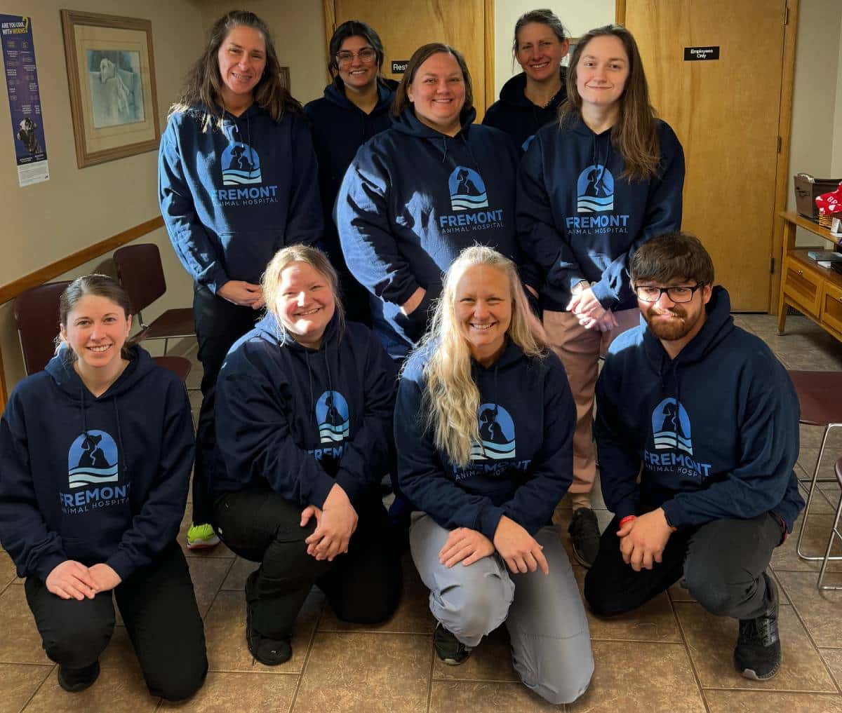 Group of nine people in matching blue hoodies smiling indoors.