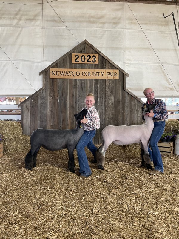 Two people posing with a black and a white lamb at the Newaygo County Fair.