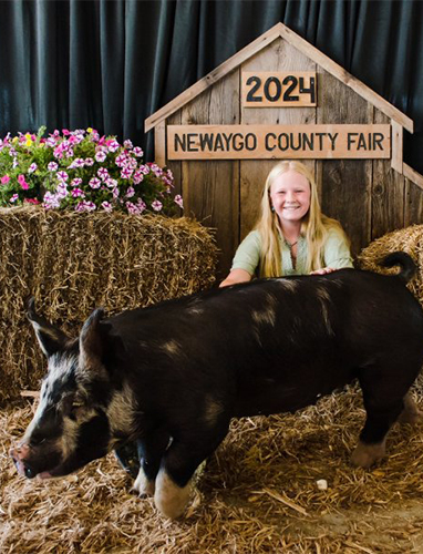 Young woman smiling behind a large black pig at the Newaygo County Fair.