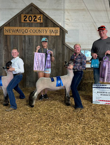 Four people proudly displaying goats and awards at the Newaygo County Fair.
